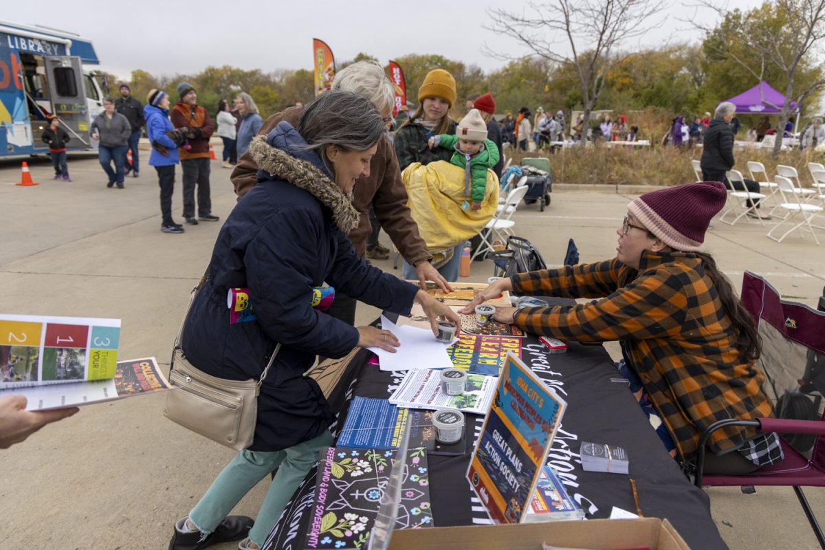 Attendees interact with a volunteer at the Indigenous Peoples Day Celebration at the Terry Trueblood Recreation Area in Iowa City on Oct. 14. The Great Plains Action Society booth had free artwork and stickers. 