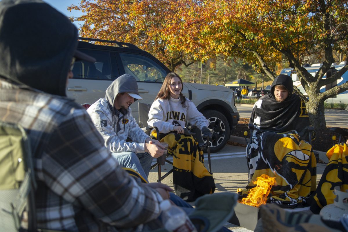 Fans warm up by a fire while tailgating at the Hancher Auditorium parking lot before the homecoming football game between Iowa and Northwestern on Saturday, Oct. 26, 2024. Temperatures dropped as low as 33 degrees in the morning.