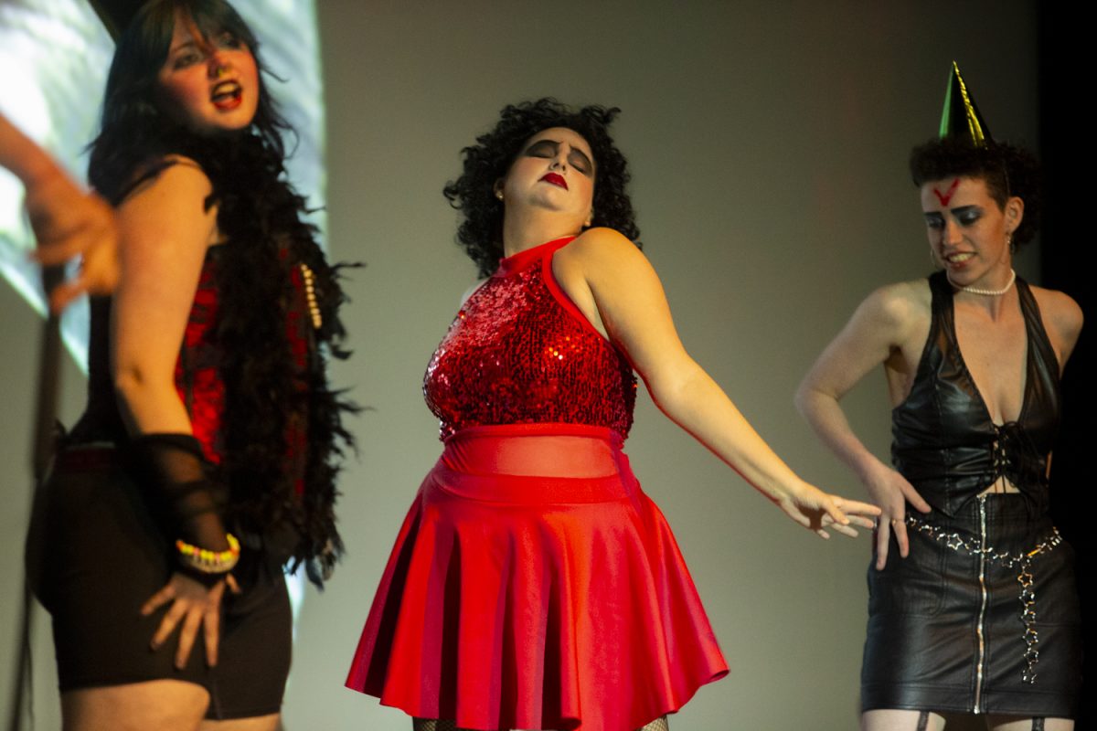 An audience member shows off their outfit onstage during the song “Time Warp” at the Rocky Horror Picture Show screening and live show at the Englert Theatre on Saturday, Oct. 26, 2024. The performance was presented by Comics in Action and props like newspapers, gloves, noisemakers, and party hats were provided for the audience to use throughout.