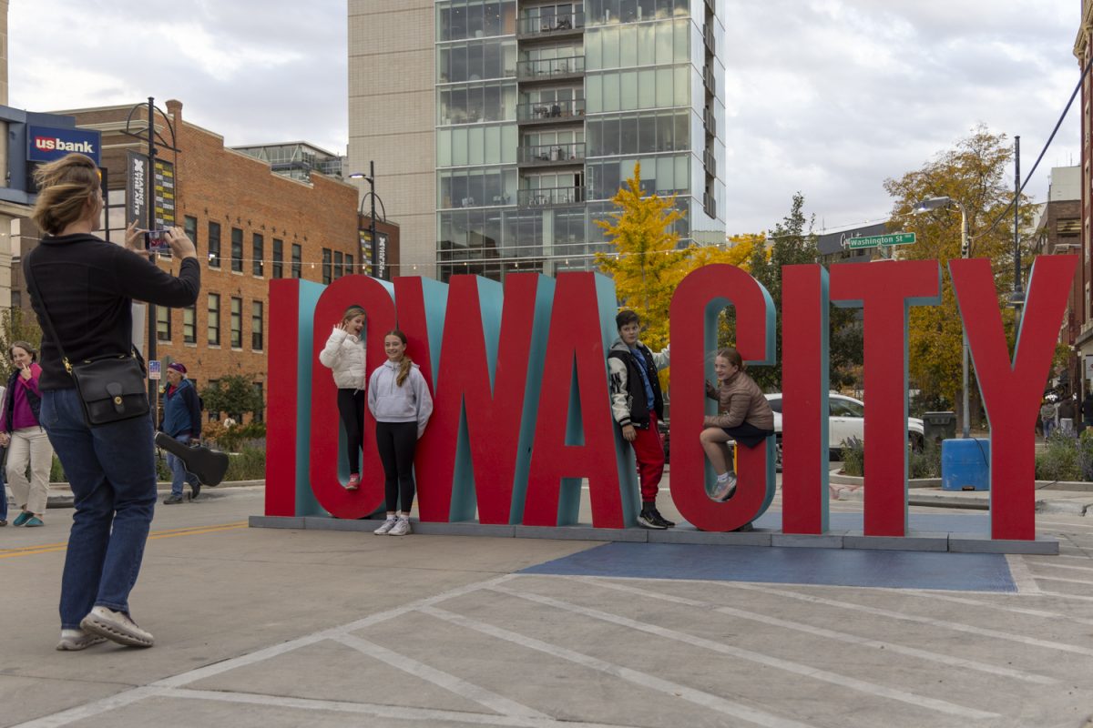 A family takes photos in front of an Iowa City sign during the Back to Dubuque Street block party in downtown Iowa City on Thursday, Oct. 24, 2024. The block party celebrated the progress of the Dubuque Street Reconstruction Project and included live music, bingo, drinks, and food.