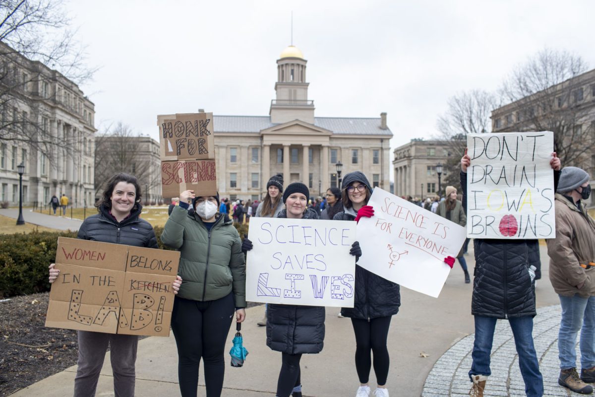 Rally goers hold up homemade posters to passersby during a Stand Up For Science rally on the Pentacrest on Friday, March 7, 2025. The rally was one of many being held nationally to protest against the Trump administration’s “censorship and political interference” in scientific research. Speakers at the event encouraged attendees to chant, cheer, and call their representatives. Live music was performed by the band Second Half.