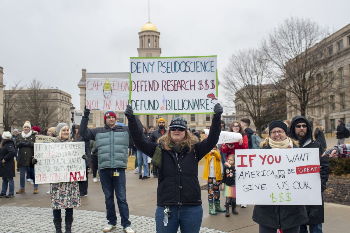 Protesters hold up homemade signs to passersby during a Stand Up For Science rally on the Pentacrest on Friday, March 7, 2025. The rally was one of many being held nationally to protest against the Trump administration’s “censorship and political interference” in scientific research. Speakers at the event encouraged attendees to chant, cheer, and call their representatives. Live music was performed by the band Second Half.
