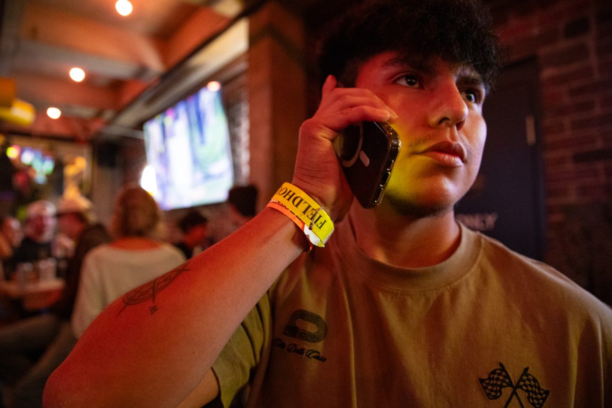 A patron makes a phone call to his friends in a Fieldhouse wristband during the opening night of Fieldhouse Bar and Grill in Iowa City on Thursday, Nov. 6, 2025. Over 100 attendees lined up down the block to drink, play arcade games, and explore the new bar’s three floors. The previous Fieldhouse was located in the Pedestrian Mall, and relocated over the summer.
