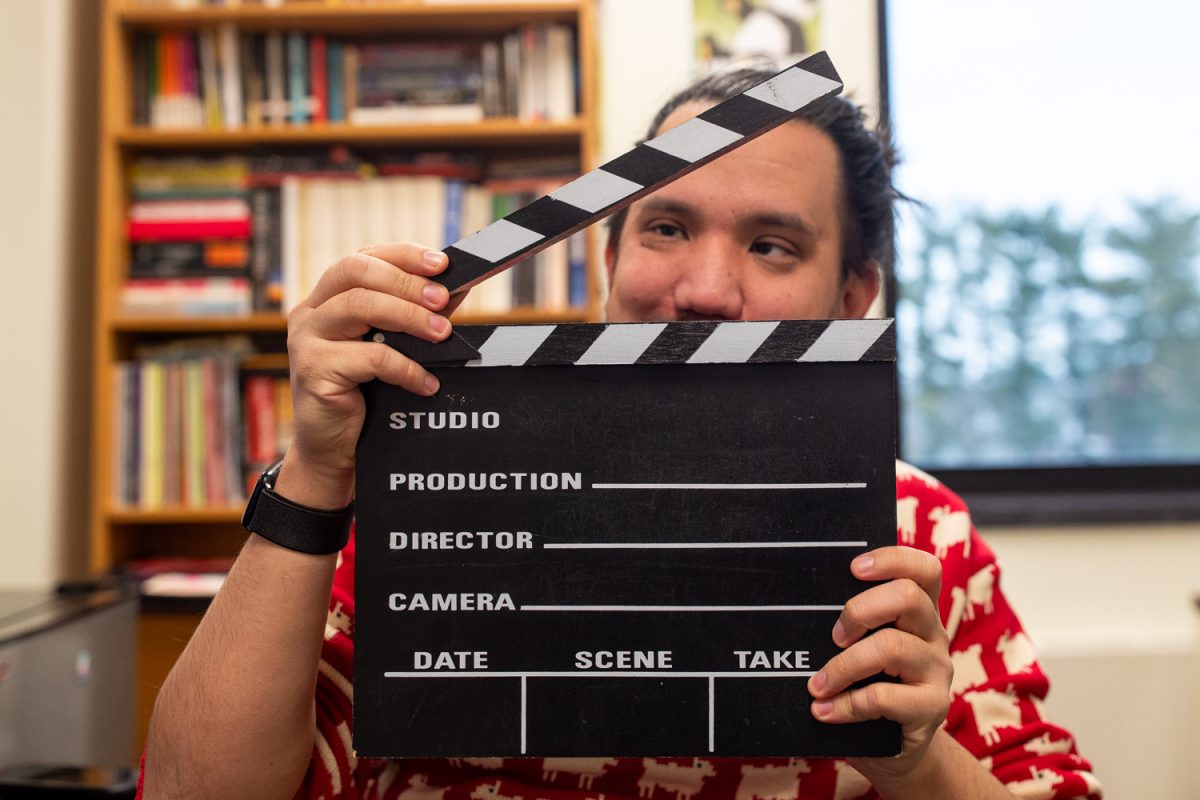 Graduate Student, Chris Wei, lifts the top of prop clapperboard in his personal office at the English Philosophy Building in Iowa City, Iowa on Monday, Dec. 8, 2025. Wei is the current Media Review professor at the University of Iowa School of Cinematic Arts. Wei gives insight on the gradual decline of constructive criticism in the media.
