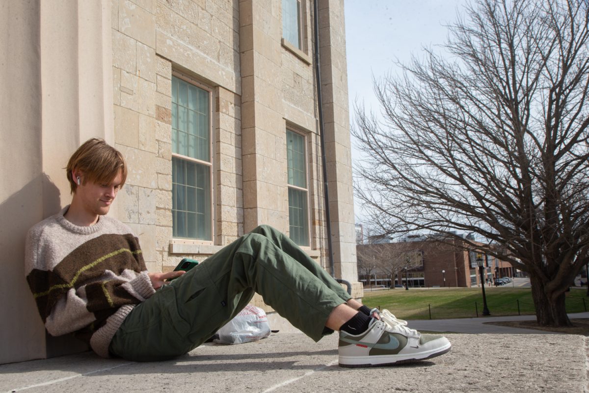 Ethan Button looks at his phone while sitting on the stairs of the Old Capitol in Iowa City, Iowa, on Tuesday, March 24, 2026.  (Sal Yang/The Daily Iowan)