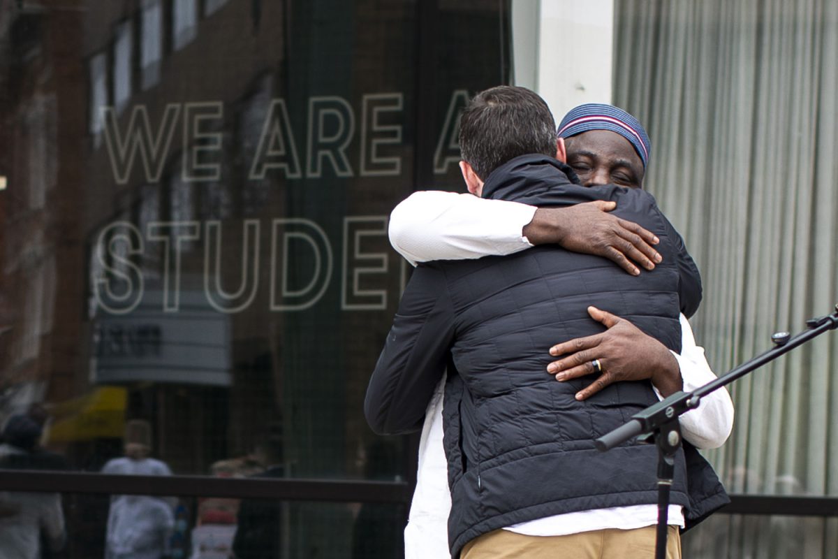 Sunday Goshit hugs Peter Gerlach, executive director of the Iowa City Foreign Relations Council, during a press conference for Goshit on the Pedestrian Mall in Iowa City, Iowa on Friday, April 3, 2026.