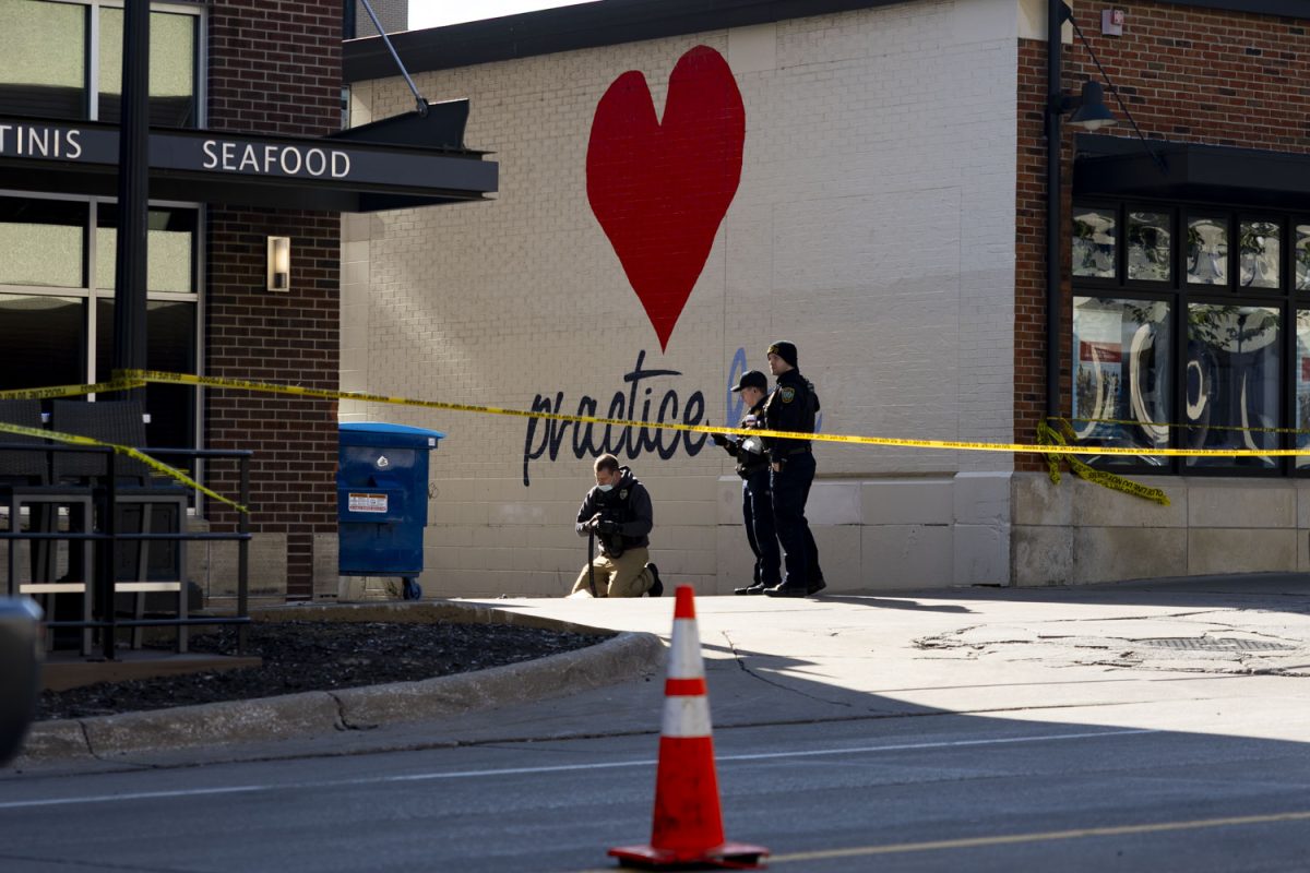 Police officers take photos in front of a Practice Love sign at a crime scene in the Pedestrian Mall Iowa City, Iowa on Sunday, April 19, 2026. Three students from the University of Iowa were injured in a shooting early Sunday morning.(Samantha DeFily/The Daily Iowan)