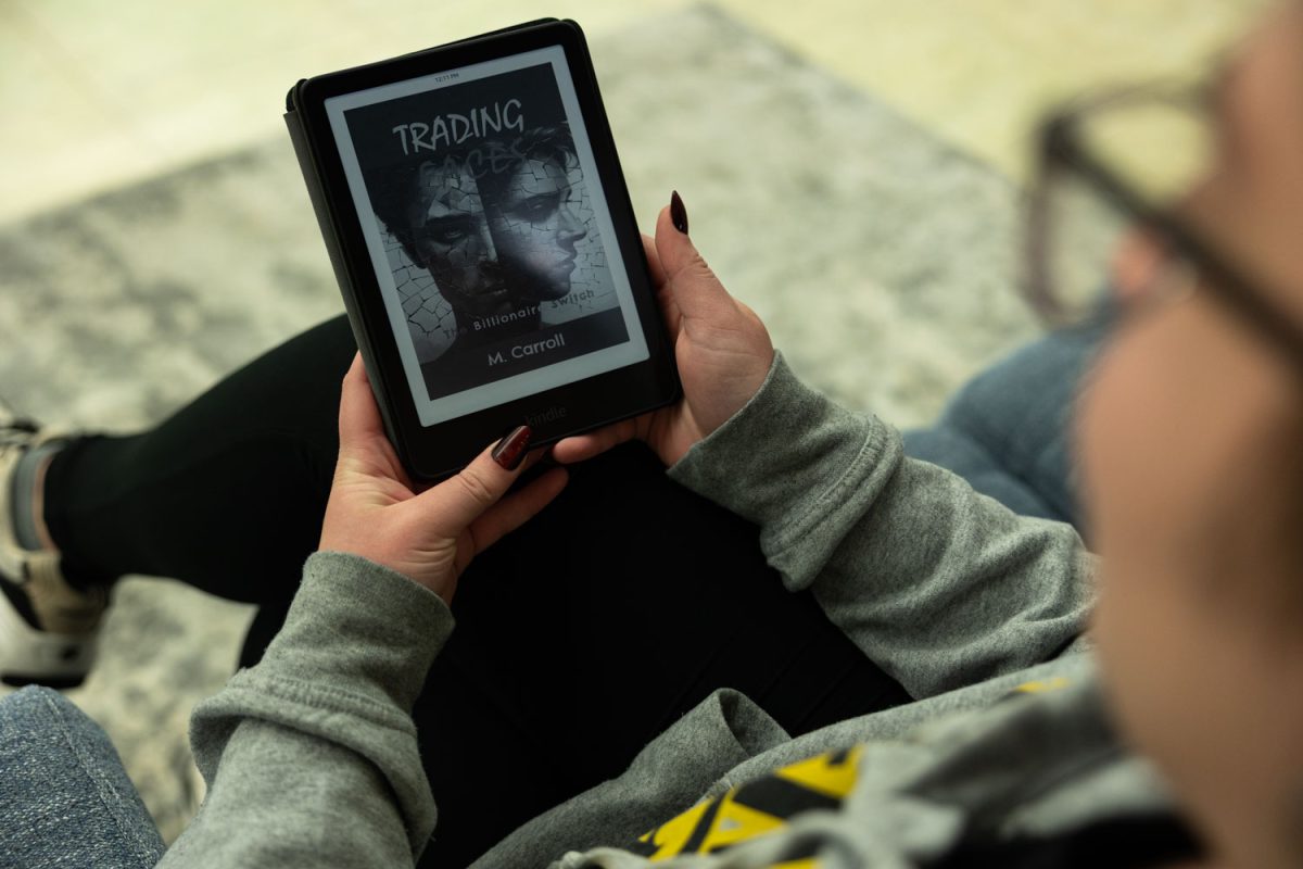 A University of Iowa student is seen reading “Trading Faces,” a novel by M. Carroll, on Monday, April 20, 2026. The novel will be released on Nov. 11, 2026. (Liz Sleper / The Daily Iowan)