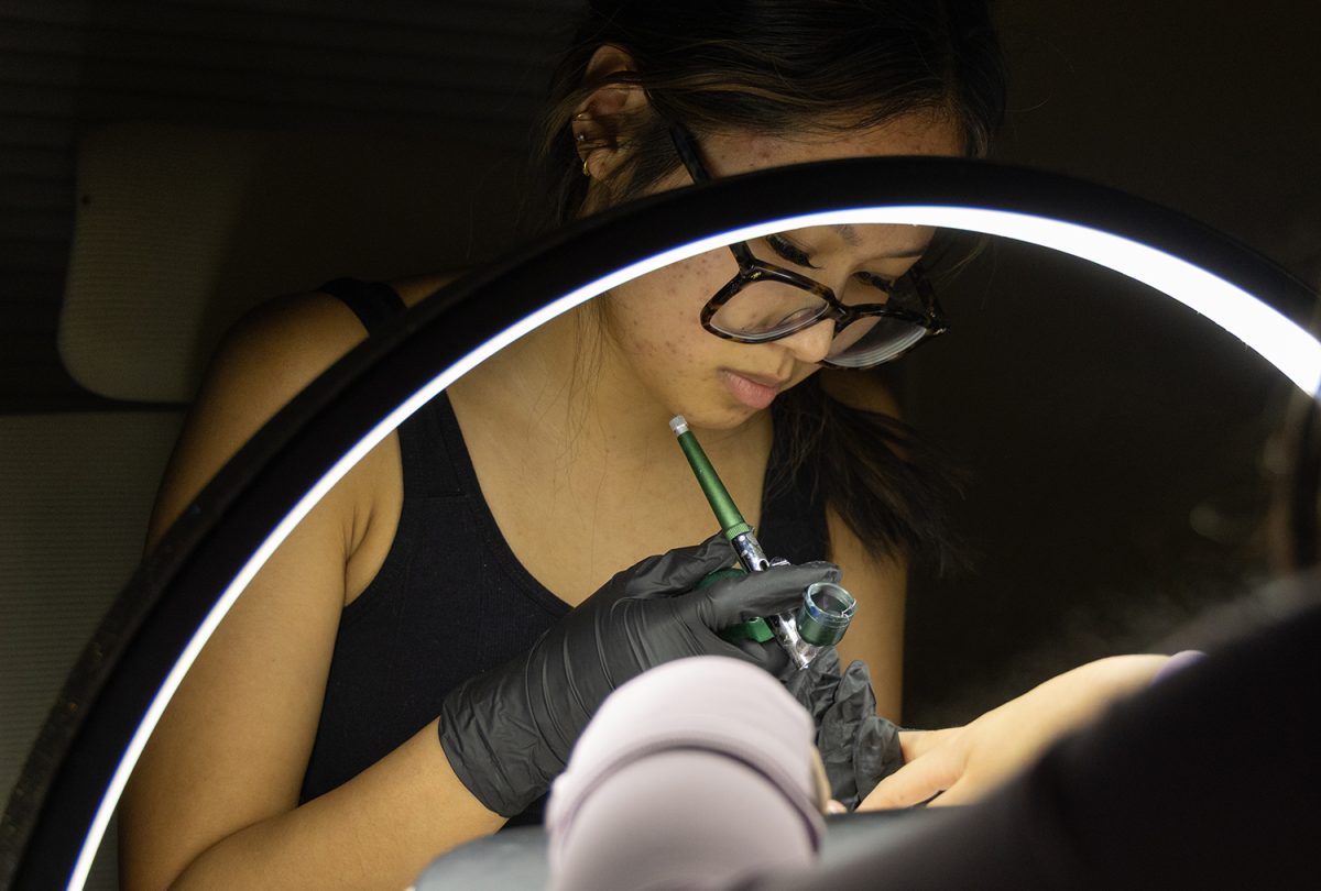 Samantha Khamphilanouvong uses an airbrush while working on a client’s manicure during an appointment on March 6, 2026, inside her apartment in Iowa City, Iowa. Khamphilanouvong balances running a small nail business with school and extracurricular commitments. (Jade Vithayasab / SJMC)