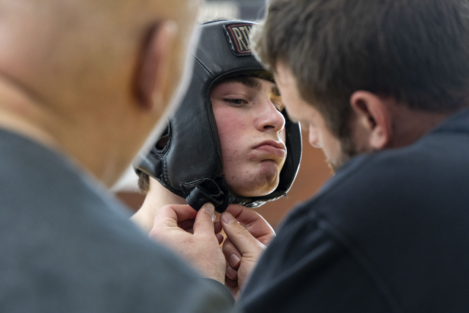 Coach Zach Knoop tightens Samson Diener’s headgear as boxing gym owner George Chamberlin watches during the Iowa State Annual Boxing Show in the State Gym at Iowa State University in Ames, Iowa on Saturday, Feb. 21, 2026. Knoop mainly trains the competitive boxing team with Chamberlin being the head of the team. (Samantha DeFily/The Daily Iowan)
